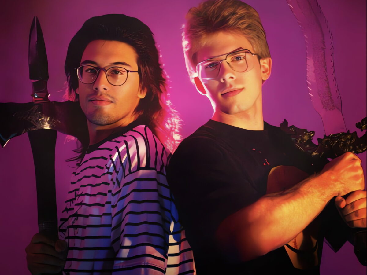 John Romero holding an axe and John Carmack holding a gun; the two are back-to-back and facing the camera against a purple backdrop