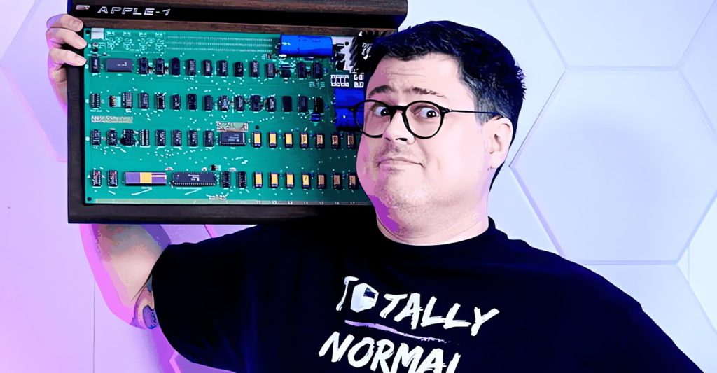A white, dark-haired, bespectacled man hoisting a motherboard on his shoulder