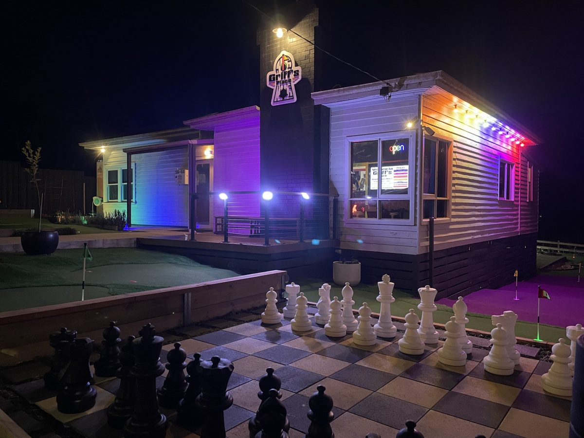 A building exterior, illuminated at night, with a giant chessboard on the lawn