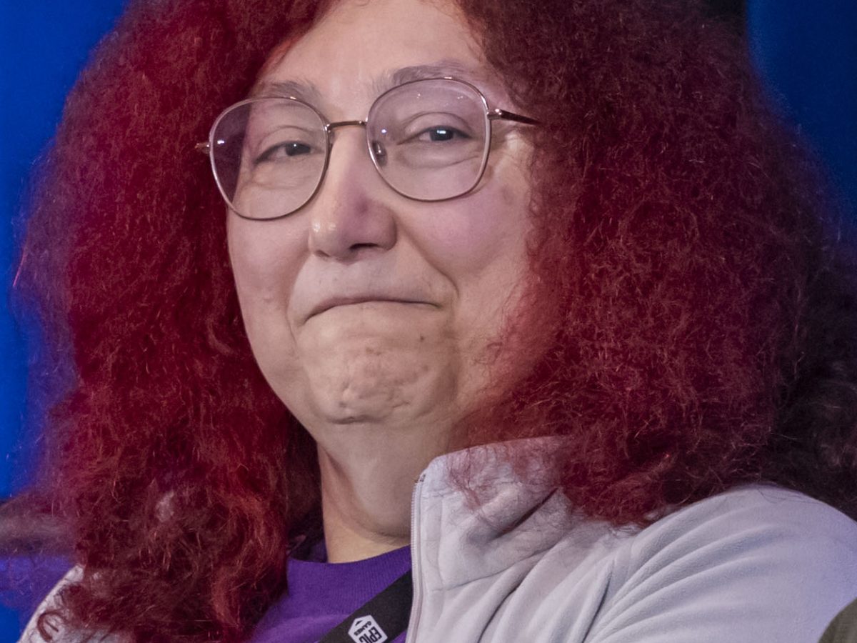 A smiling, red-haired white woman with glasses