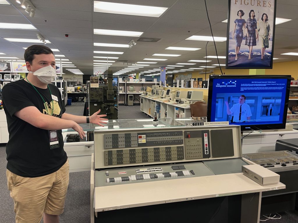 A masked young man shows off a 1960s computer terminal