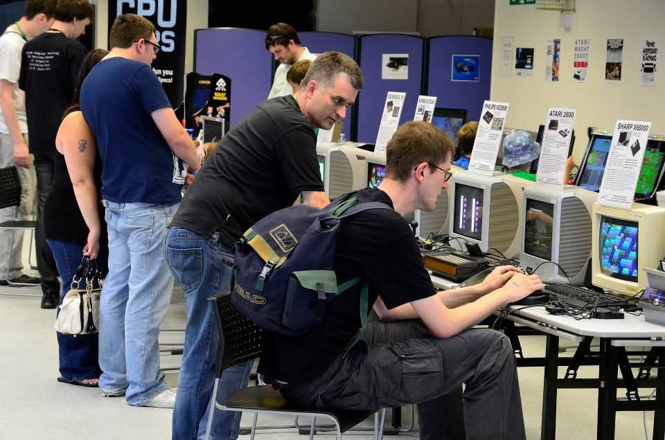 Profile shot of one guy sitting at an old computer on a table full of retro computers