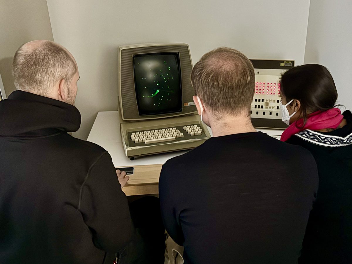 Three masked people sitting in front of a retrocomputer